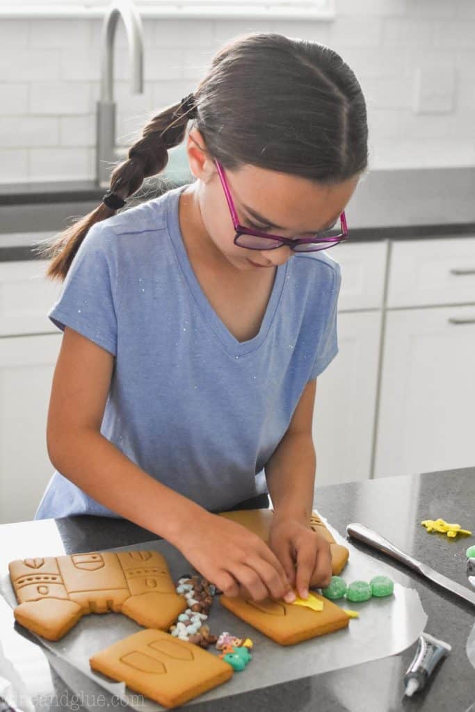 little girl with glasses and braids decorating a cookie castle with yellow fondant 