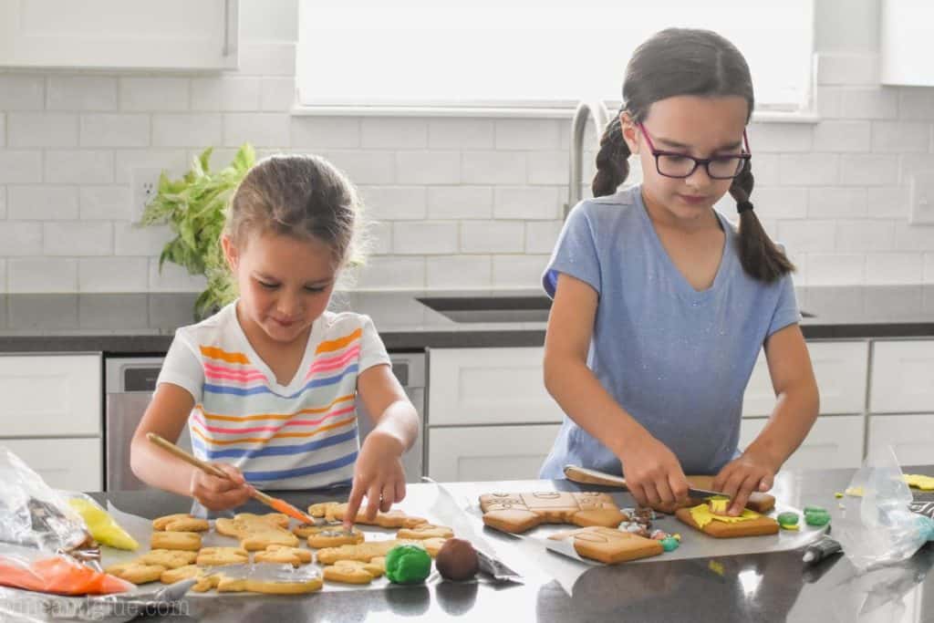 two little girls standing at a counter decorating cookies 