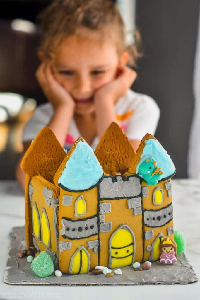little girl in the background looking at a decorated gingerbread castle cookie creation