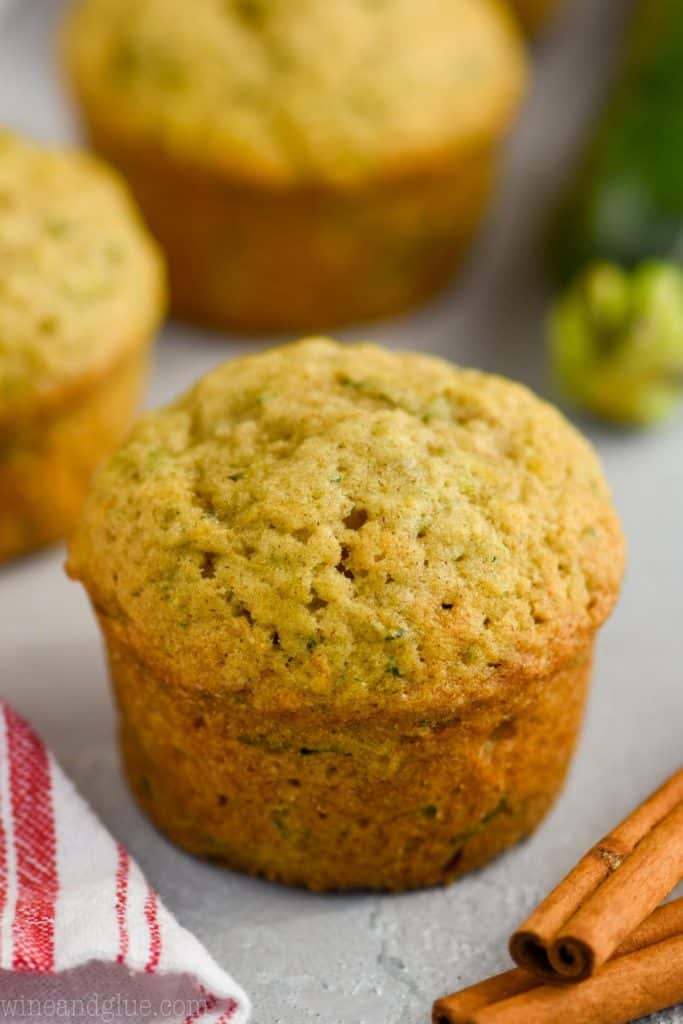 a zucchini muffin with cinnamon sticks next to it and a cloth napkin, whole zucchini in the background