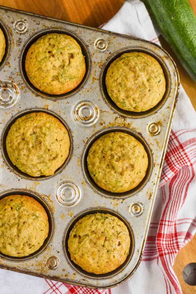 overhead view of zucchini muffins in an old fashioned muffin tin on top of a red checked napkin