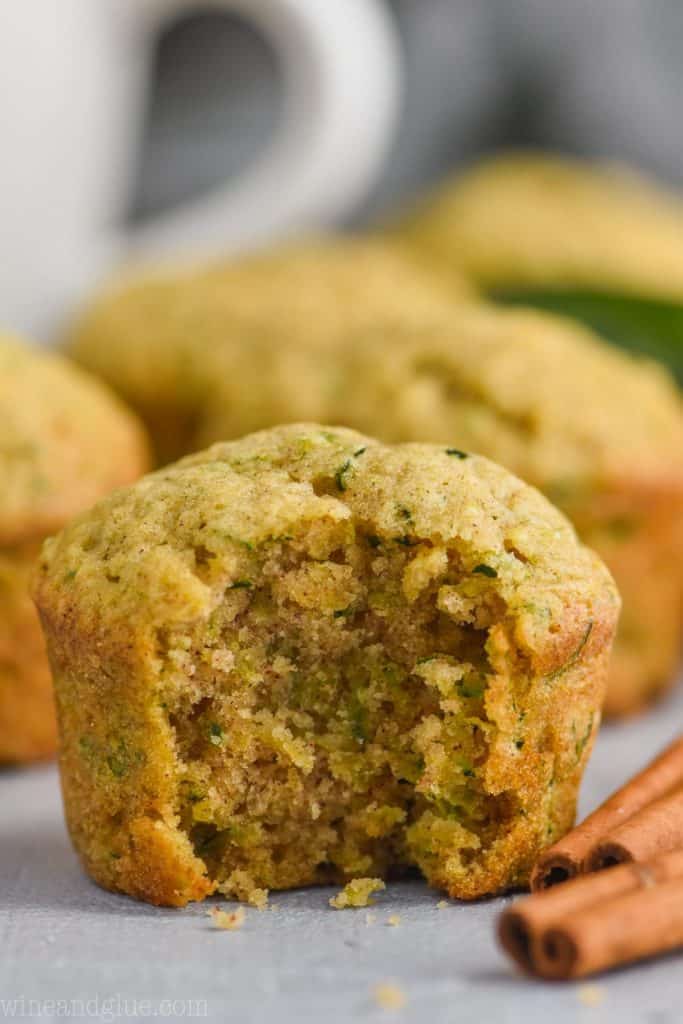 close up picture of a zucchini muffin with a bite out of it and two cinnamon sticks on the side.