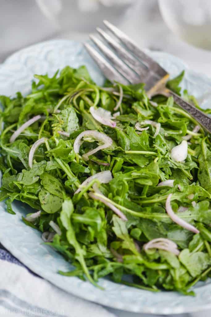close up view of an easy arugula salad recipe with thin slices of shallot on a teal plate 