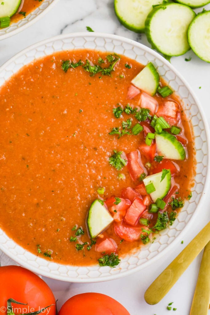 overhead picture of a bowl of gazpacho with cucumbers, tomatoes, and parsley on top