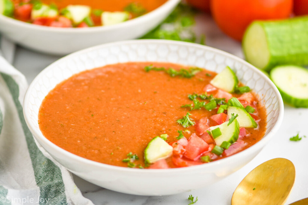 landscape photo of a bowl of gazpacho soup with cucumber and tomato on top