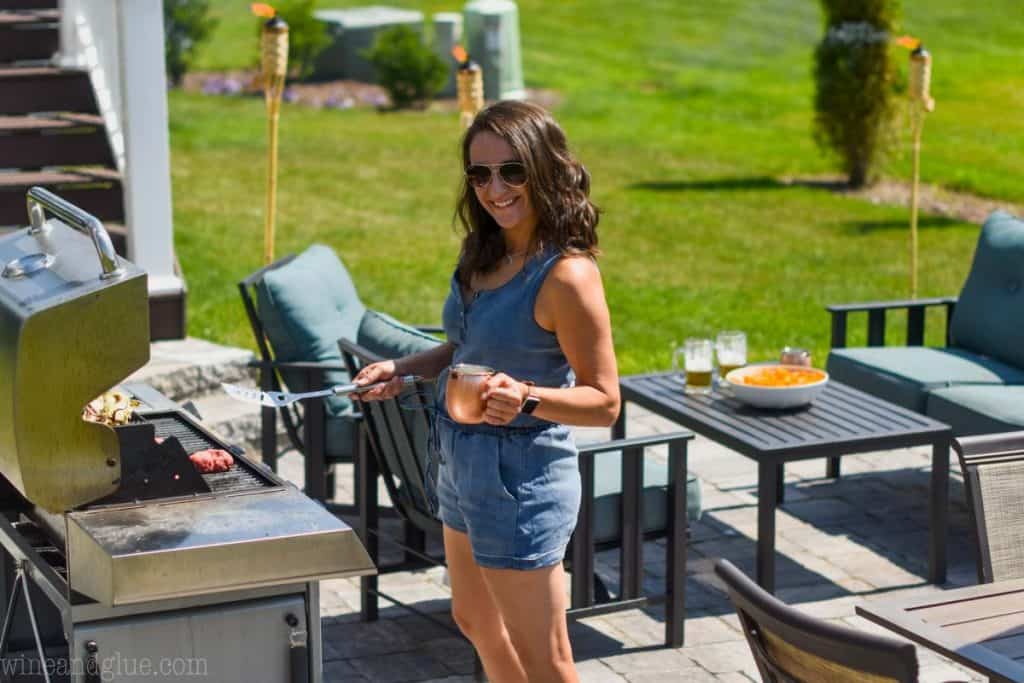 woman standing outside by a grill, holding a cocktail