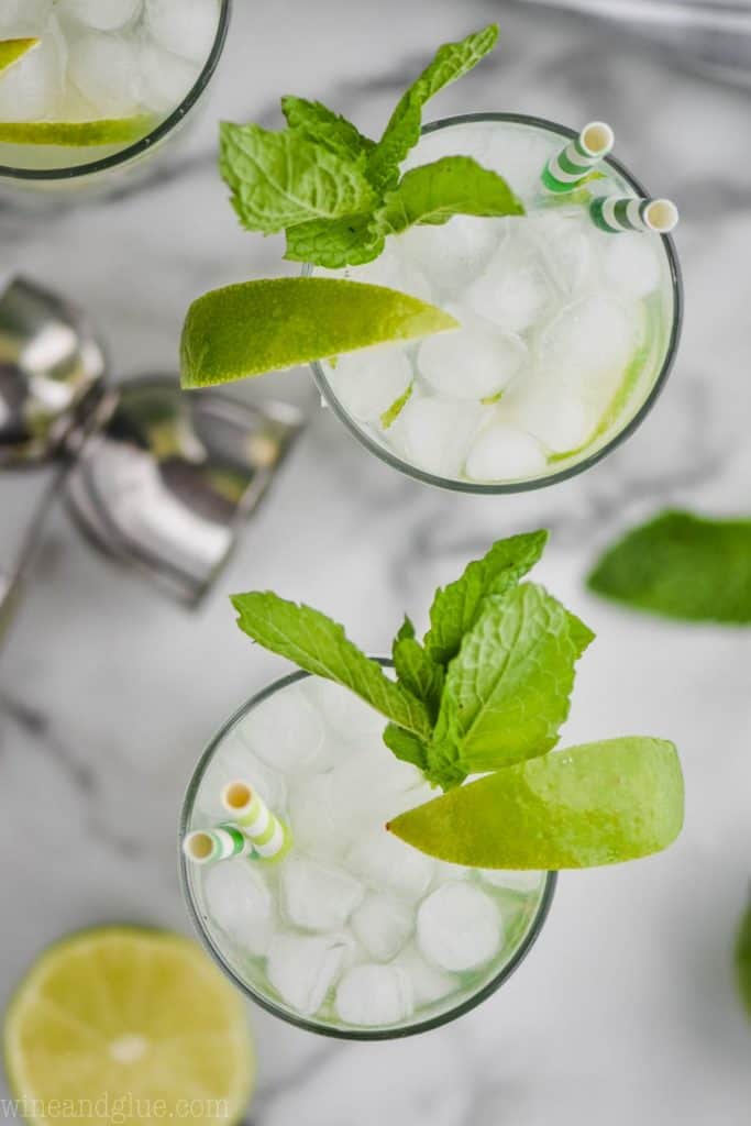 overhead view of two highball glasses filled with the best mojito recipe, ice, lime wedges, and fresh mint