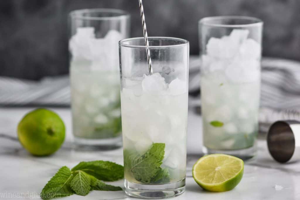 three glasses filled with ice with the first one being mixed by a long spoon to make a mojito