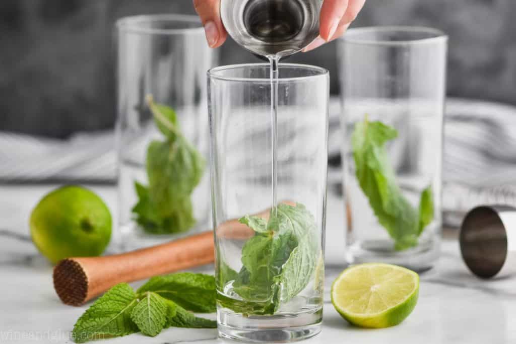 three high ball glasses with mint leaves in them and simple syrup is being poured into the first glass