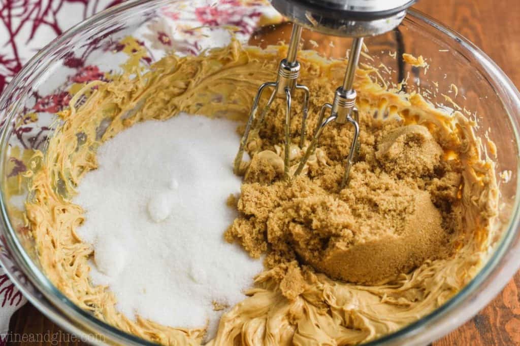 white and brown sugar being added to the batter of pumpkin peanut butter cookies with the beaters of a hand mixer being put into the bowl