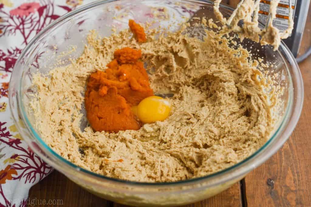 pumpkin puree and an egg yolk being added to pumpkin peanut butter cookie batter in a large glass bowl