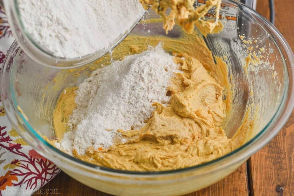 flour being poured into a bowl of pumpkin peanut butter cookie batter