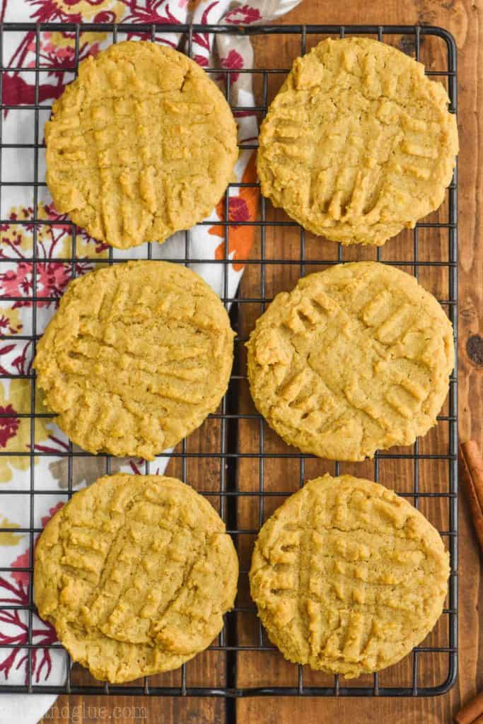 six pumpkin peanut butter cookies on a cool rack (overhead view), a fall themed cloth napkin underneath on a wood board