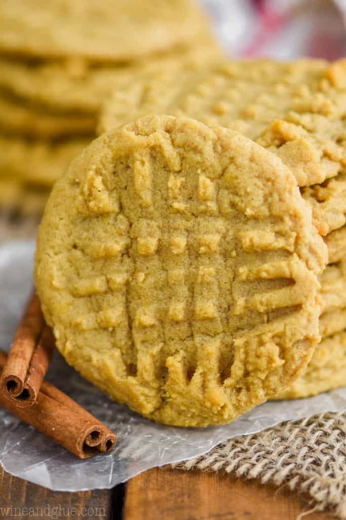 front view of a pumpkin peanut butter cookie as it leans against a stack of cookies, a second stack in the background