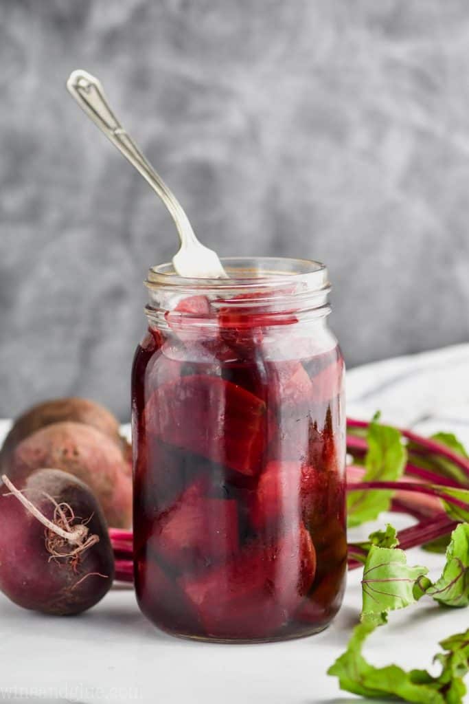 fork sticking out of an open mason jar of pickled quick pickled beets on a white surface against a gray background