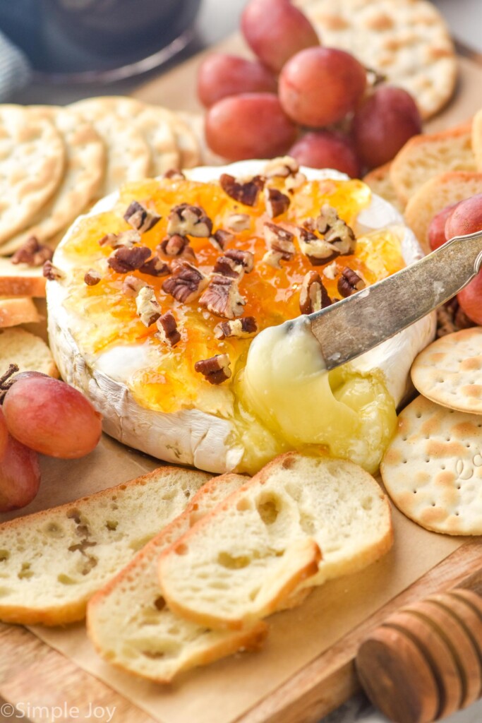 brie cheese topped with marmalade, honey, and pecans being pulled out with a knife