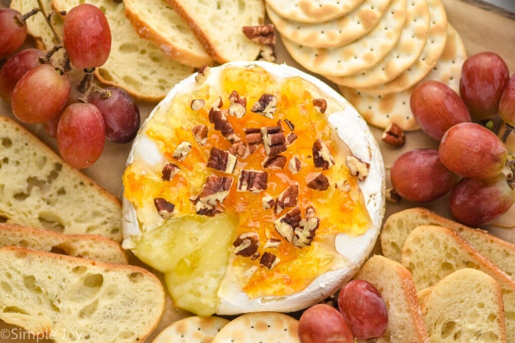 overhead of a wheel of brie on a platter with honey, marmalade, and pecans with cheese coming out