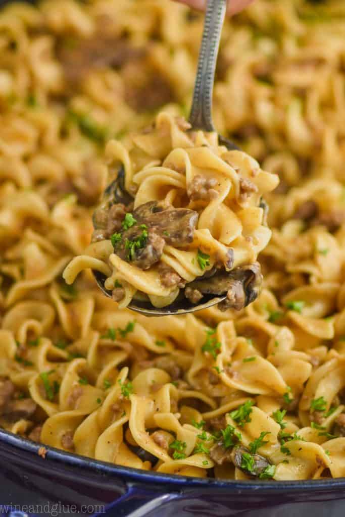 serving spoon dishing up ground beef stroganoff recipe with egg noodles, sliced mushrooms, and fresh parsley
