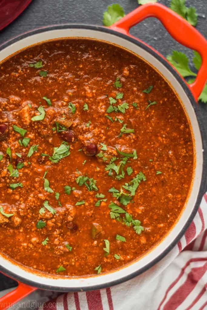 overhead view of a red stock pot filled with vegetarian chili and garnished with cilantro on a black surface top