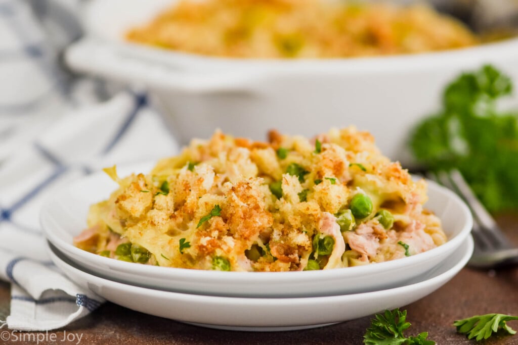 landscape photo of two white plates stacked with easy tuna casserole on it and casserole dish in the background