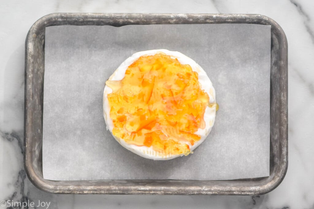 overhead of a wheel of brie with marmalade and honey on a parchment paper lined baking sheet