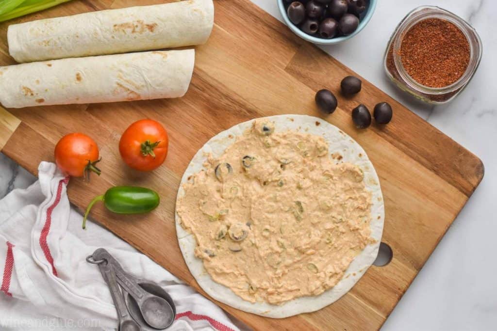 the filling for taco pinwheel appetizer spread out on a tortilla shell sitting on a cutting board