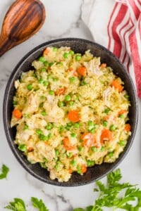 overhead photo of a black bowl full of instant pot chicken and rice, fresh parsley off to the side and a serving spoon