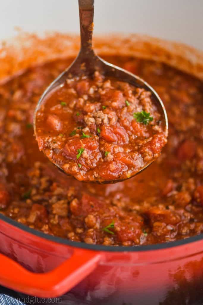 red dutch oven with meat sauce being ladled out, garnished with a little parsley