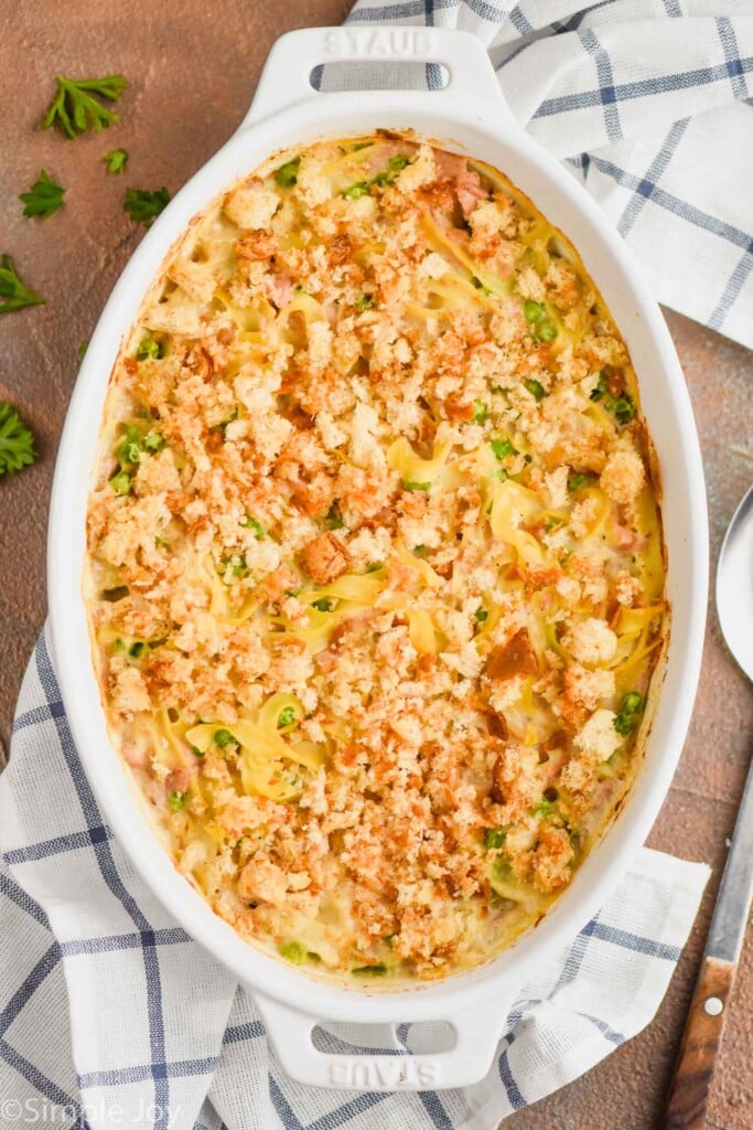 overhead view of oval casserole dish full of tuna casserole and garnished with parsley on a white cloth napkin with blue stripes