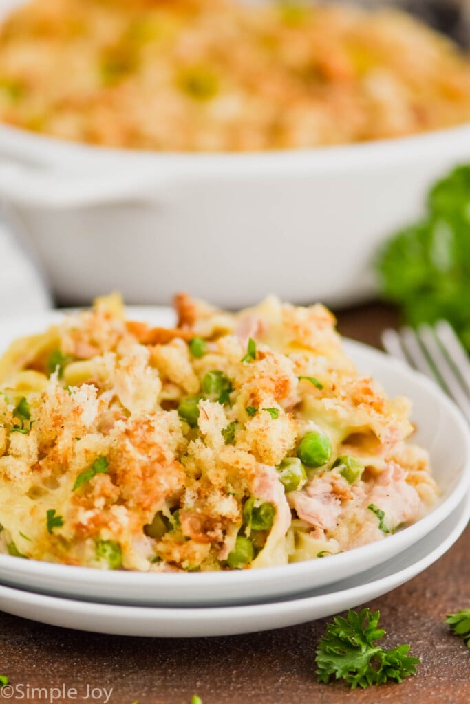 two white plates stacked with a heaping serving of tuna casserole recipe on top and the dish in the background