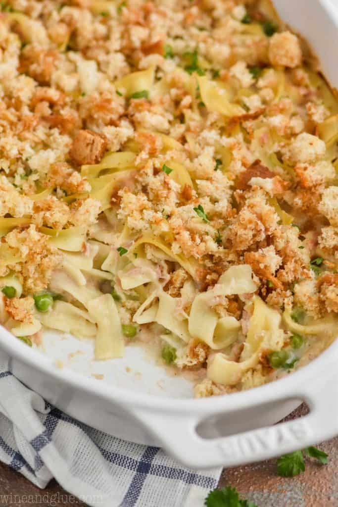 a white casserole dish full of tuna noodle casserole with a spoonful missing