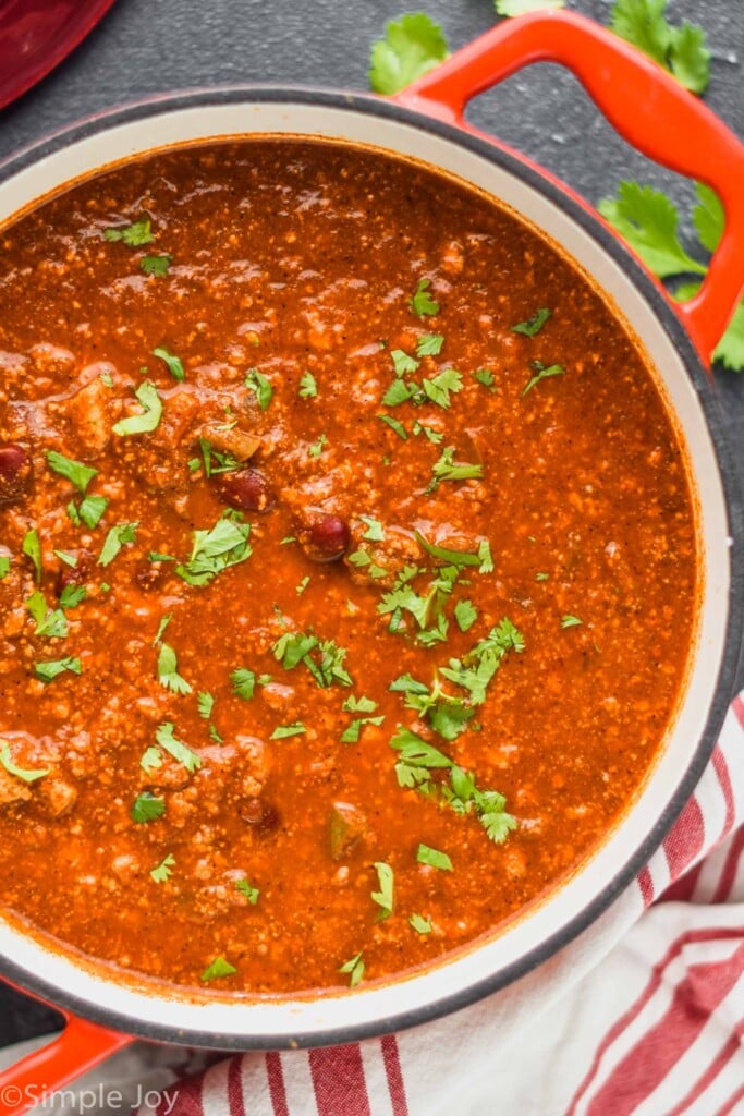 overhead view of a red stock pot filled with vegetarian chili and garnished with cilantro on a black surface top