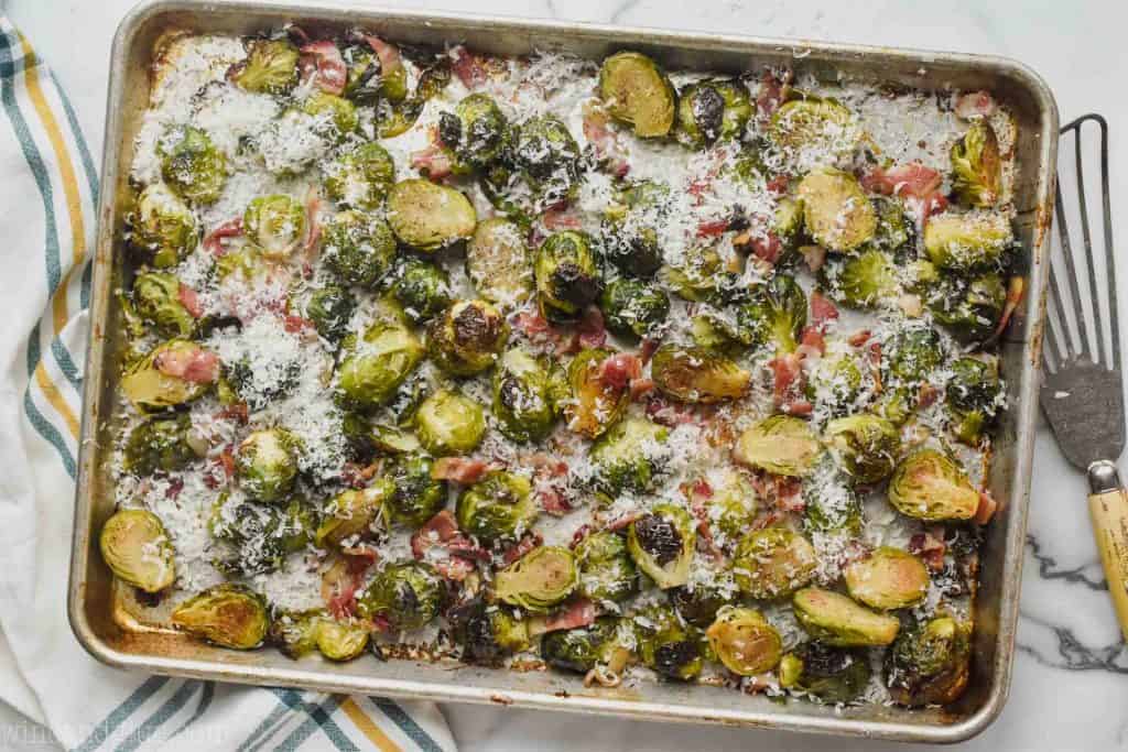 overhead photo of rimmed bacon sheet with roasted brussels sprouts, cooked bacon, and garnished heavily with freshly shaven parmesan cheese