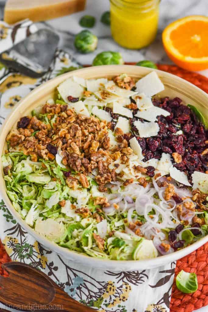 white wooden bowl with brussel sprouts salad with cranberries, shaved parmesan, walnuts and thinly sliced shallots