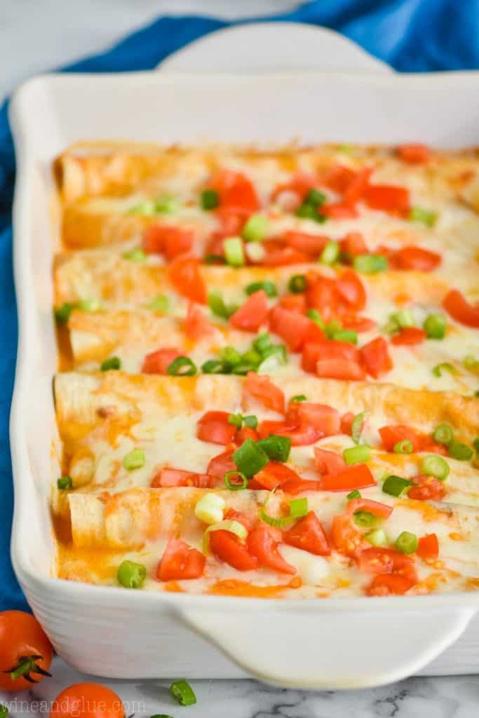 side view of a chicken enchilada casserole in a white ceramic baking dish, enchiladas are buffalo flavored and garnished with chopped tomatoes and green onions