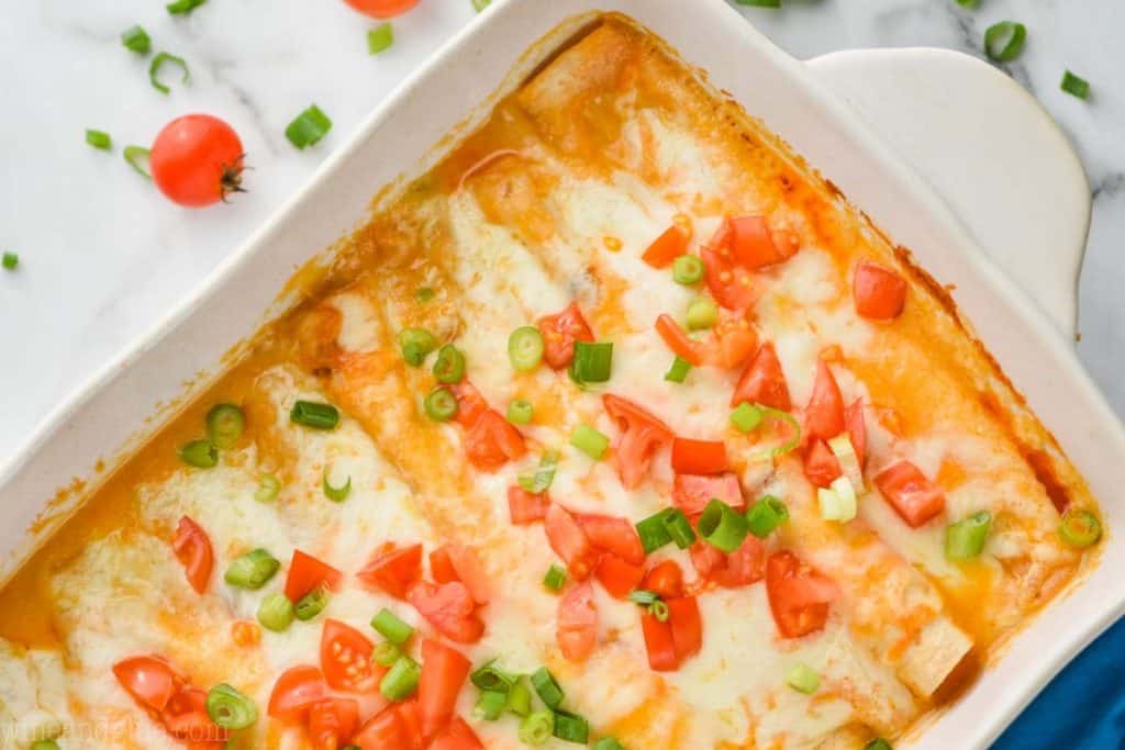 landscape view of a white ceramic baking dish filled with chicken enchiladas (buffalo flavored) garnished with green onions and chopped tomatoes