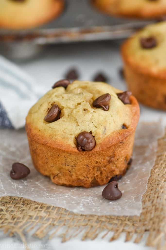 a single banana chocolate chip muffin sitting on wax paper with chocolate chips around it