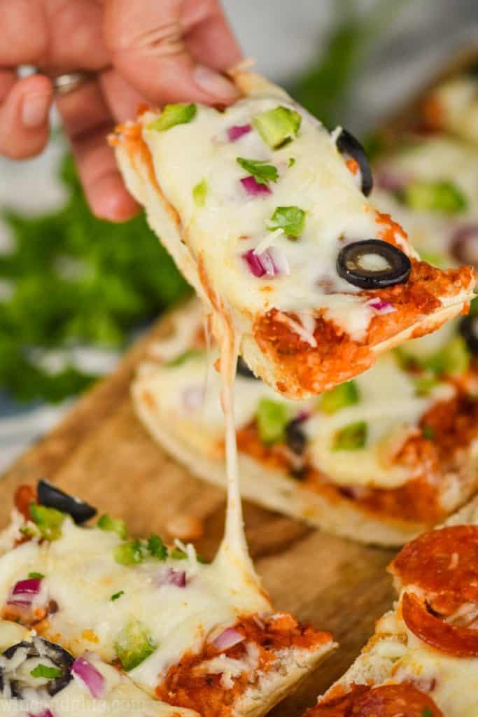 a piece of homemade french bread pizza topped with olives and peppers being pulled from the rest