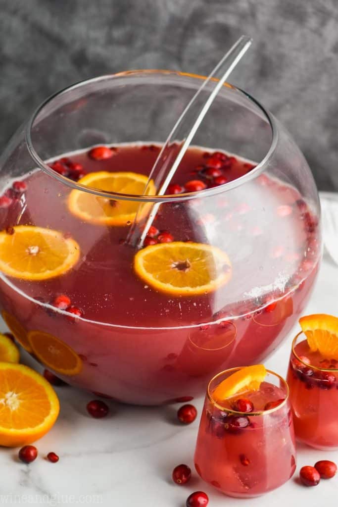 a sphere punch bowl full of red holiday punch recipe with cranberries and orange slices floating in it