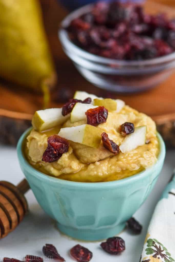 light teal bowl filled with hummus and topped with honey, pear pieces, and dried cranberries