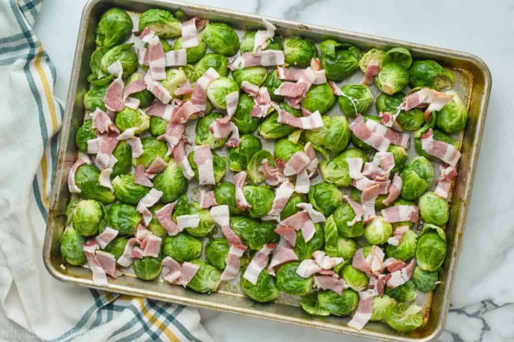 overhead photo of a rimmed baking sheet with raw brussels sprouts - all the cut sides down - and raw bacon pieces on top