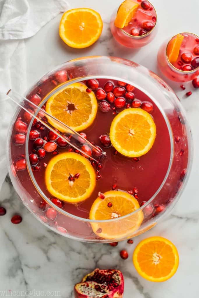 overhead view of sphere punch bowl with non alcoholic Christmas punch with orange slices and cranberries floating in it and two glasses full of it