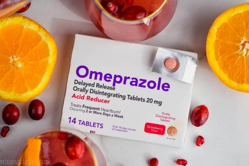 overhead view of a box of omeprazole with one pill tablet on top and ingredients for holiday punch around it