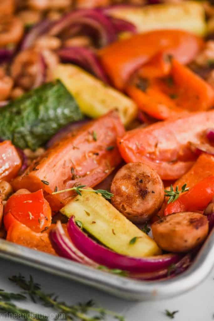 up close view of sausage and veggie sheet pan dinner recipe with zucchini, tomatoes, peppers, cut chicken sausages and red peppers on a rimmed baking sheet