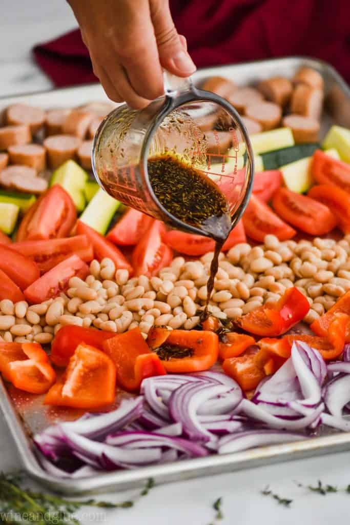 pouring a marinade over sheet pan dinner with beans, vegetables, and chicken sausages