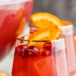 pinterest graphic of a gold rimmed wine glass full of non alcoholic holiday punch with cranberries floating in it and an orange wedge, says: the best holiday punch