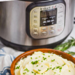 pinterest graphic of mashed potatoes made in the instant pot in a wooden bowl sitting in front of an instant pot, with a cloth napkin next to it, says: instant pot mashed potatoes simplejoy.com