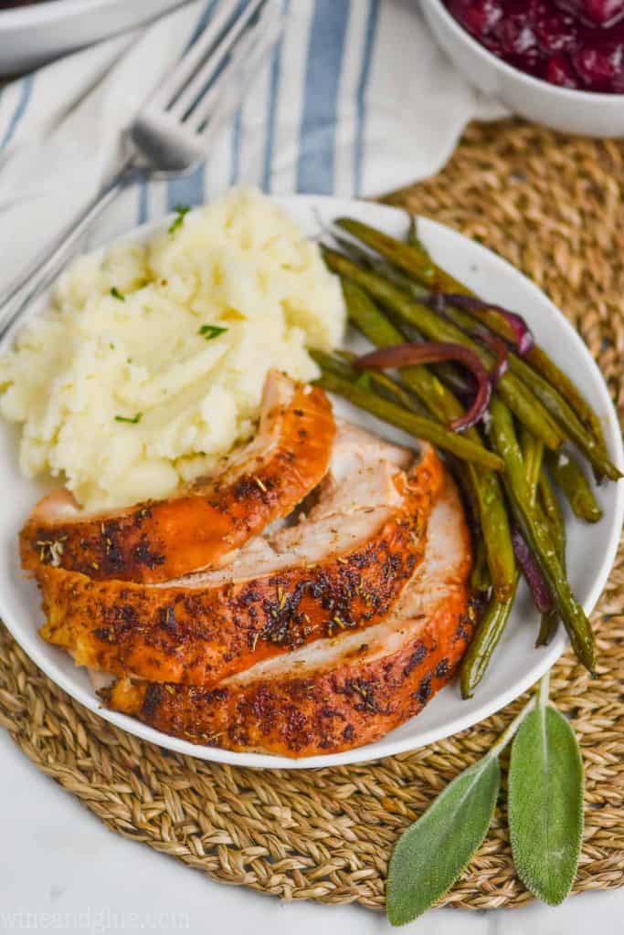 cut up baked turkey breast on a plate with mashed potatoes and green beans