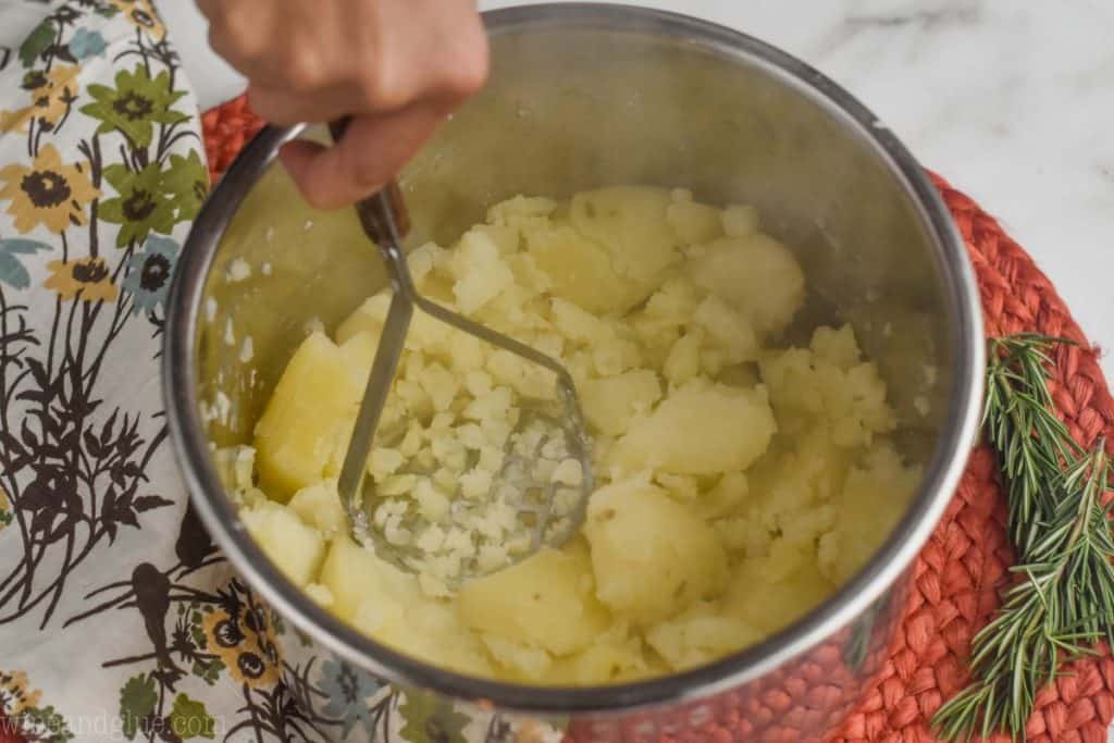 a hand mashing cooked potatoes that are in an instant pot