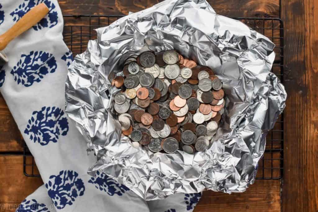 overhead view of a pie crust (unseen) in a pie plate that has been lined with aluminum foil and has lots of loose change in it